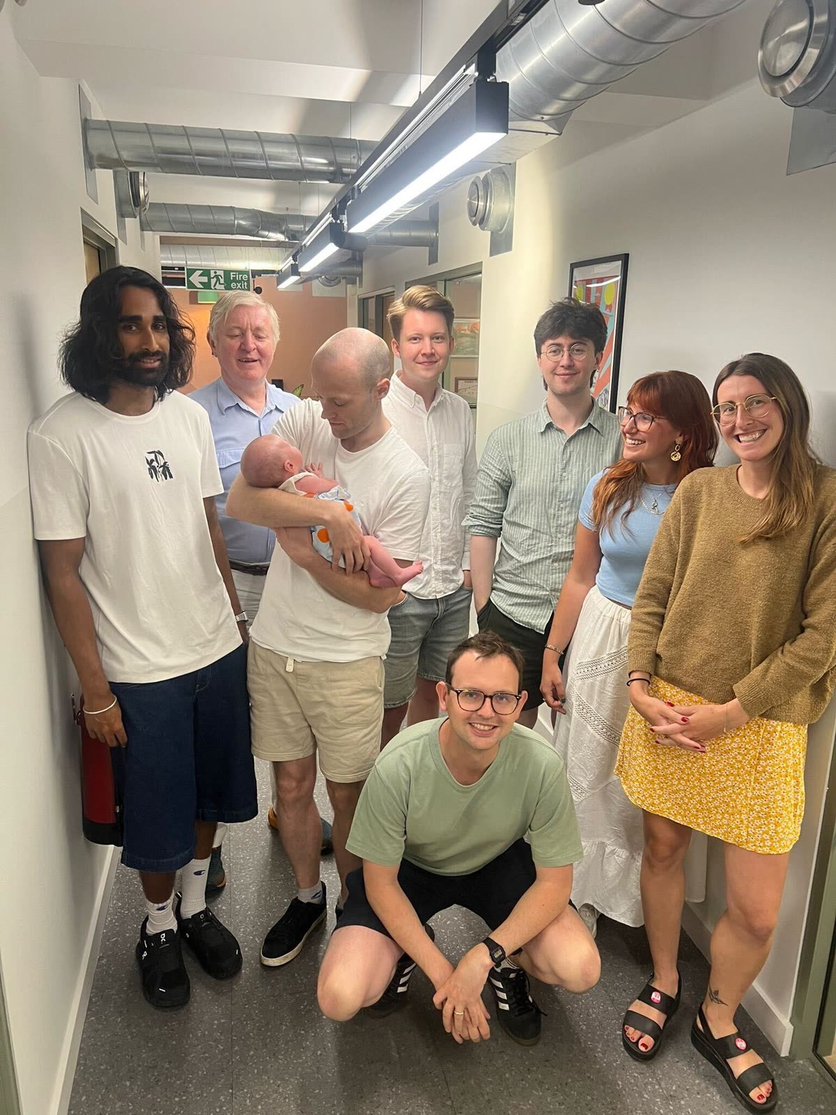 The Plinth team gathered in the office with a colleague holding a newborn baby